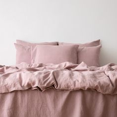 an unmade bed with pink linens and pillows on the headboard, in front of a white wall