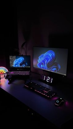 two computer monitors sitting on top of a desk next to a keyboard and mouse in the dark