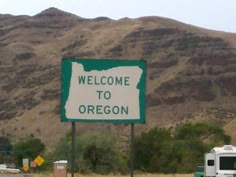 a welcome to oregon sign on the side of the road with mountains in the background