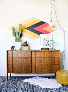 a living room with a rug, wooden furniture and colorful artwork on the wall above it