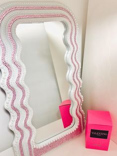 a pink vase sitting next to a white mirror