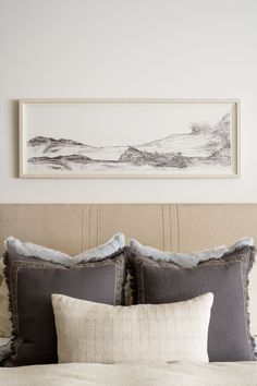 a bed with two pillows on top of it and a painting above the headboard