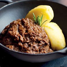 a close up of a bowl of food with meat and potatoes on the side,