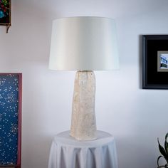 a white lamp sitting on top of a table next to a painting and potted plant