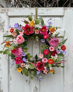 a wreath is hanging on an old white door with pink, yellow and red flowers