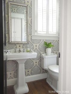 a white toilet sitting next to a bathroom sink under a mirror on top of a wooden floor