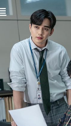 a young man wearing a white shirt and green tie standing in front of a desk