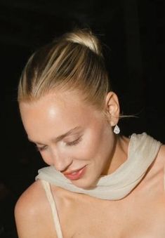 a woman with her eyes closed wearing a white shirt and earrings, looking down at her cell phone