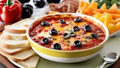 a bowl of black olives and cheese dip surrounded by sliced bread, tomatoes, bell peppers, crackers, and pepperoni