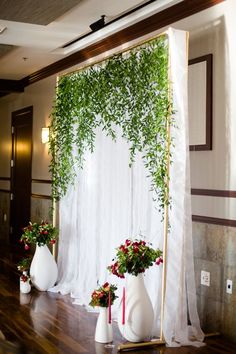 an arrangement of flowers and greenery on display in front of a white drape