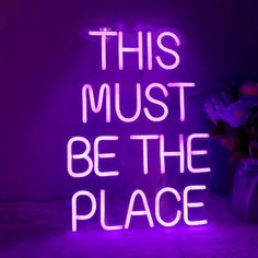 a neon sign that says, this must be the place in front of a vase with flowers