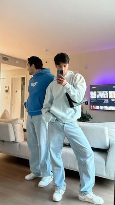 two young men standing in front of a couch looking at their cell phones