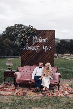 a man and woman sitting on a couch in front of a sign that says always always you