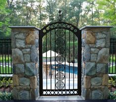 an iron gate in front of a pool with trees and bushes behind it, surrounded by stone walls