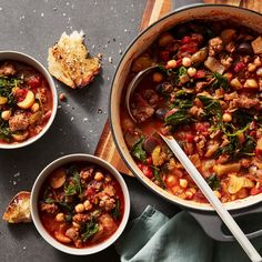 two bowls filled with stew next to bread on top of a wooden cutting board and spoons