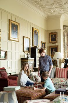 three people are sitting in a living room with couches and paintings on the walls