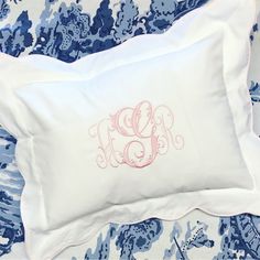 an embroidered monogrammed pillow on top of a blue and white floral bed spread