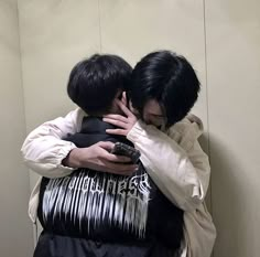 two young men hugging each other while standing in front of a wall with their arms around one another