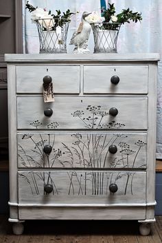 an old dresser with flowers painted on the drawers and knobs is sitting in front of a window