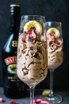 two wine glasses filled with ice cream and toppings next to a bottle of booze