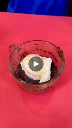 a red bowl filled with pudding on top of a pink tablecloth covered table next to a person