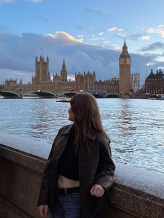 a woman standing on the edge of a bridge next to a body of water with big ben in the background