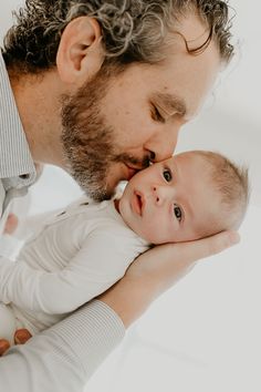 a man kisses his baby's forehead while he is holding it in his arms