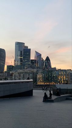 people are sitting on benches in front of the cityscape at sunset or dawn