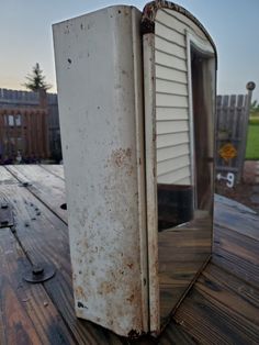 an old white refrigerator sitting on top of a wooden deck next to a fence and building