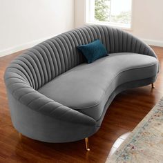 a curved couch with a blue pillow on it in front of a rug and window