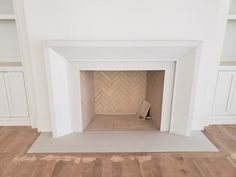 an empty room with white walls and wood flooring in the center is a fireplace