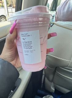 a woman holding up a pink drink in her car