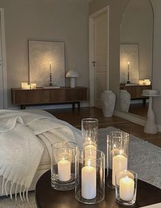 candles are lit on a table in front of a bed with white blankets and pillows