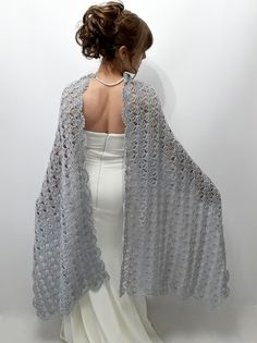 a woman in a white dress is wearing a gray crocheted shawl with an open back