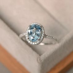 an oval blue topaz ring sits in a box with its lid open and the diamond band around it