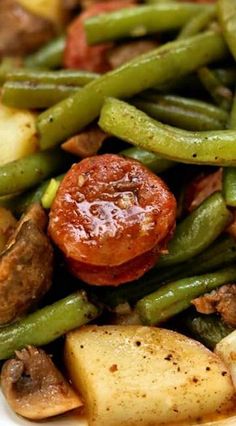 a white plate topped with green beans, potatoes and sausage covered in seasoning sauce