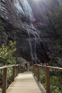 a wooden walkway leading to a waterfall with people standing at the bottom and below it