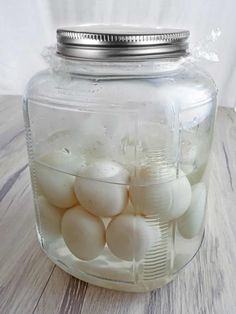 a glass jar filled with white eggs on top of a wooden table