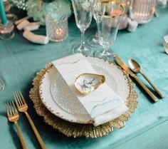 the table is set with gold and white plates, napkins, silverware, and flowers