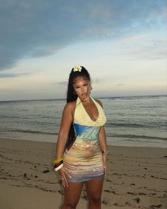 a woman standing on top of a sandy beach next to the ocean with her hand in her mouth