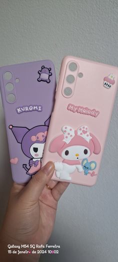 someone holding up two cell phones with cartoon characters on them, one is pink and the other is purple