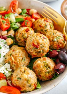 a white bowl filled with meatballs and salad next to a fork on top of a table