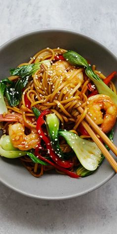 a bowl filled with noodles, vegetables and chopsticks on top of a table