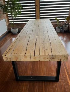 a wooden table sitting on top of a hard wood floor next to potted plants