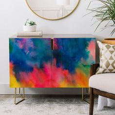 a colorful painted cabinet next to a chair and potted plant in a living room