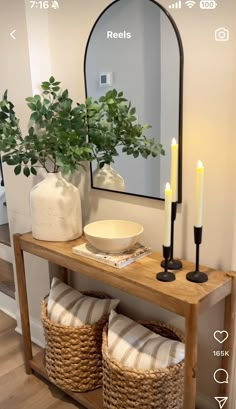 a wooden table topped with a vase filled with flowers next to a mirror and two wicker baskets