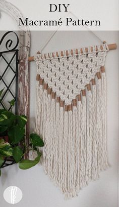 a macrame wall hanging made with yarn and wooden pegs on a white wall next to a potted plant