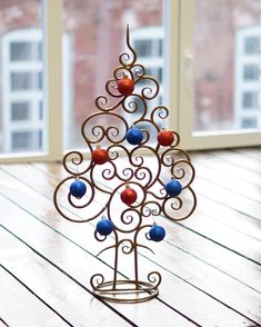 a small metal christmas tree with ornaments on it's stand in front of a window