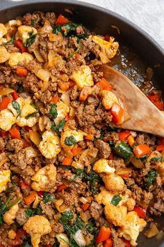 a skillet filled with meat and vegetables on top of a white countertop next to a wooden spoon