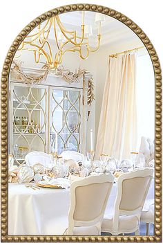 a dining room table with white chairs and a gold framed mirror in the middle of it